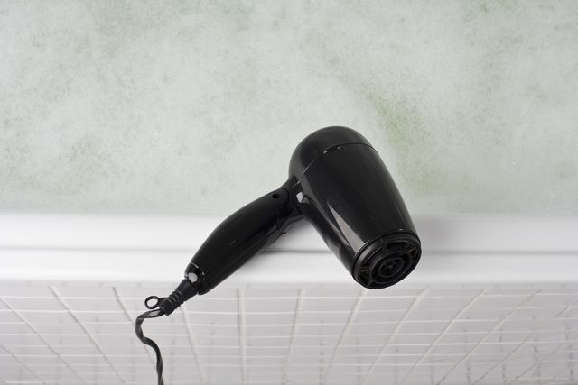 a hair dryer balancing on the edge of a full bathtub