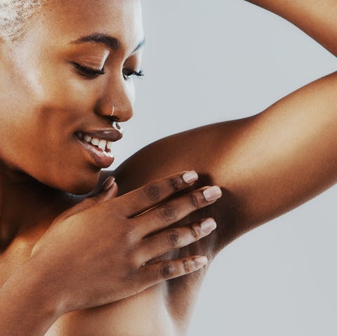 cropped shot of an attractive young woman standing alone and touching her underarm against a gray background in the studio