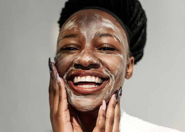 lachende vrouw die een gezichtsmasker op haar huid smeert