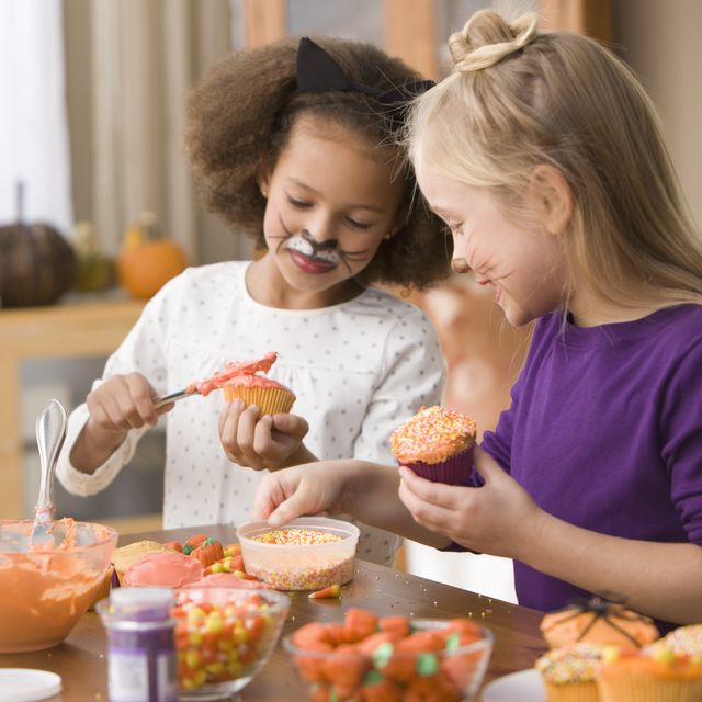 girls in halloween costumes decorating cupcakes