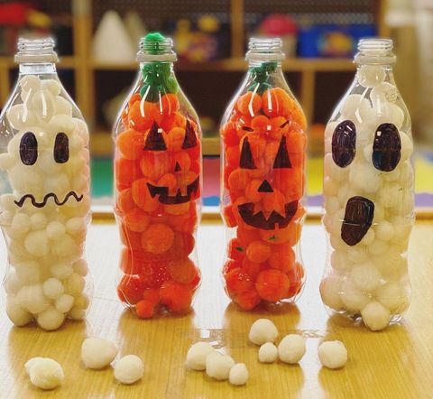plastic bottles with ghost or jackolantern face drawn on, filled with white or orange pompoms as halloween craft for toddlers