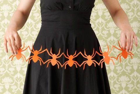 woman in black dress holding row of orange paper spider cutouts