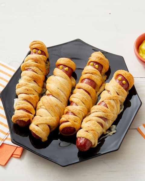mummy hot dogs on black plate with mustard