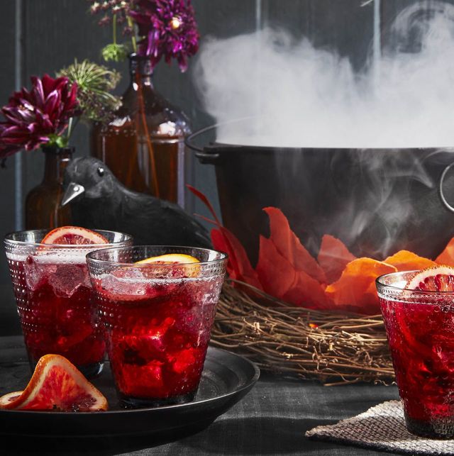 halloween punch pomegranate rum punch with orange garnish in glasses by a dutch oven cauldron smoking with dry ice