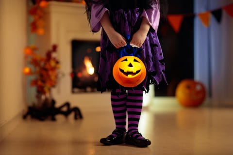 little girl in witch costume on halloween trick or treat at home pumpkin and candle decoration of fireplace dressed up child trick or treating kid holding candy bucket kids celebrate halloween