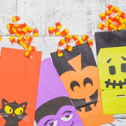 candy corns ready for packing in craft paper halloween bags on white wooden background