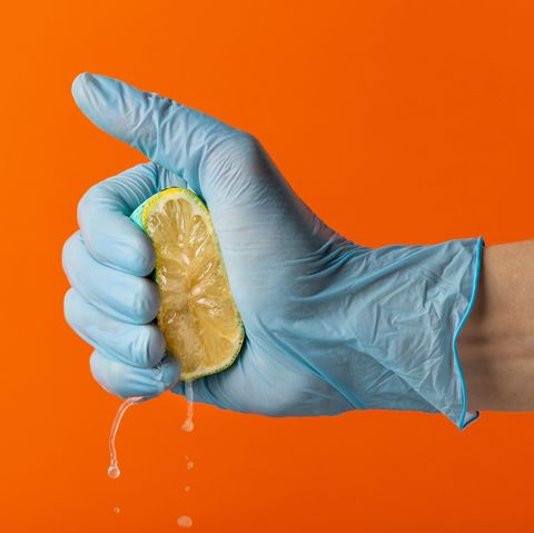 Hand in blue glove squeeze lemon on an orange background. Copy space. Close-up