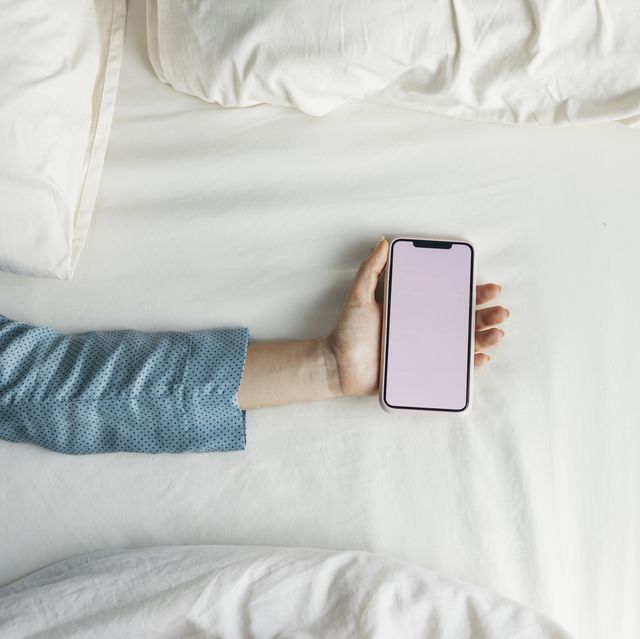 sleeping apps hand of a woman in pyjamas holding a smartphone on the bed