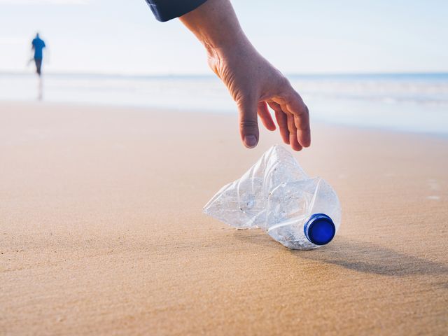 hand picking up plastic bottle at beach