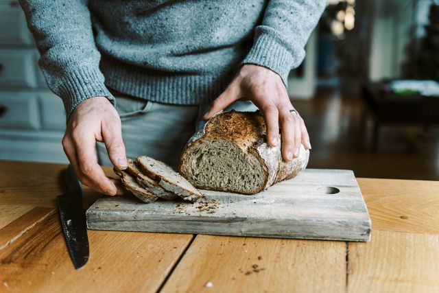 hands of a man holding and cutting a rustic sourdough bread with knife