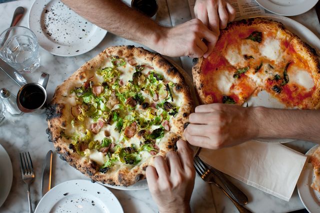 hands reach for naples style pizza