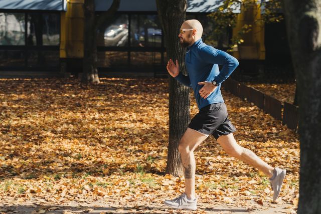 handsome bald athlete wearing sunglasses running outdoors on a warm autumn day, with leaves all around