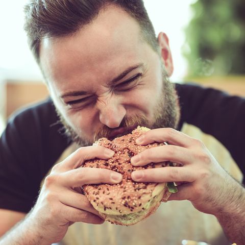 Handsome Male Eating A Cheeseburger In Fast Food Restaurant