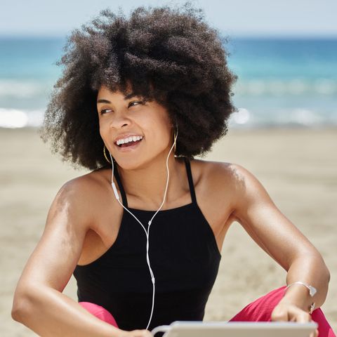 Happy afro american woman listening music on beach looking away