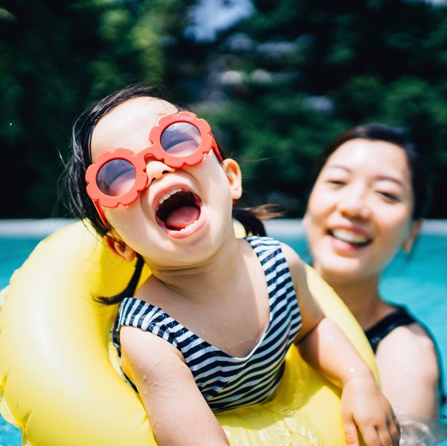 Happy Asian toddler girl with sunglasses smiling joyfully and enjoying family bonding time with mother having fun in the swimming pool in summer