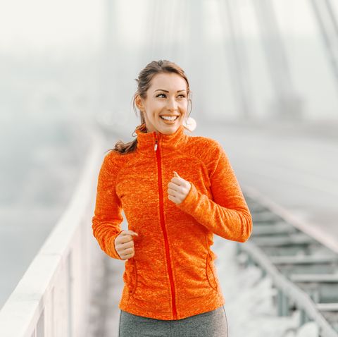 happy caucasian woman in sportswear and with ponytail running on the bridge at winter