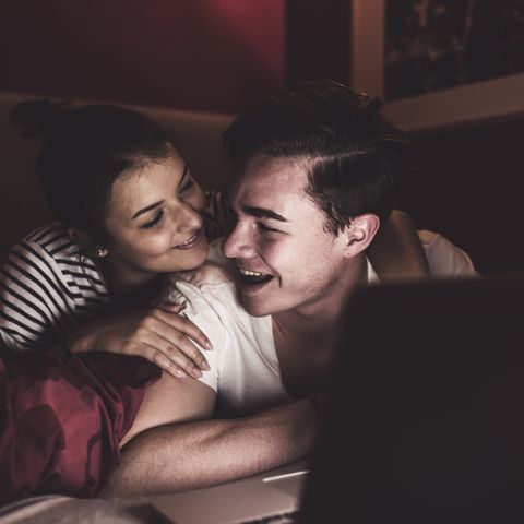 Happy couple lying in bed at home with laptop