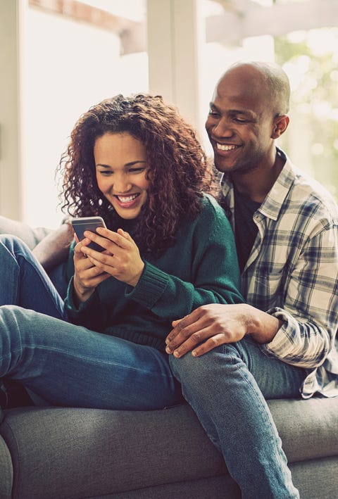 happy couple using smart phone on sofa at home