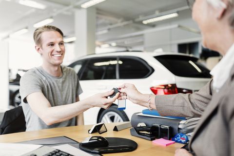 happy man receiving car keys from saleswoman at desk in showroom