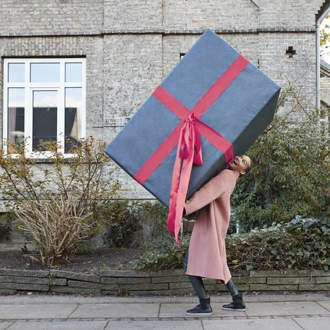 happy woman carrying large gift box on footpath