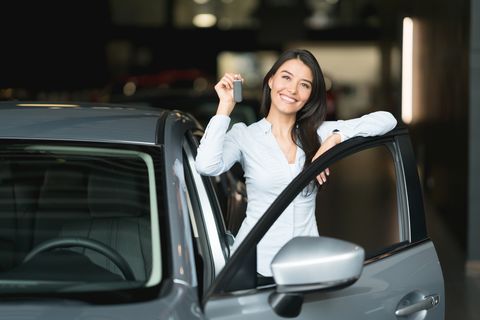 Happy woman holding keys to her new car at the dealership