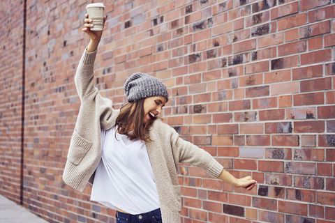 happy woman with coffee to go singing and dancing on the street