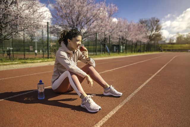 happy young female athlete eating an apple on sports track