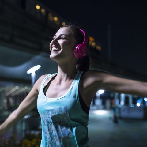 happy young woman with pink headphones listening to music in modern urban setting at night