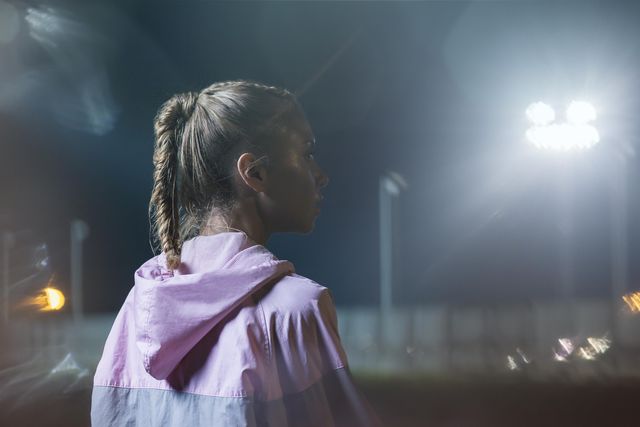 portrait of a female urban runner at night, midshot, looking away from camera, low key bokeh background, landscape composition, backlit, one female only aged 24 to 28