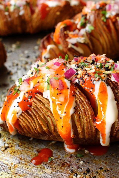 closeup of a hasselback potato topped with cream cheese, hot sauce, red onions, and everything bagel seasoning