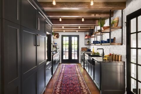 galley kitchen with white walls, black cabinets, wood floors and red runner rug facing french doors to the outside