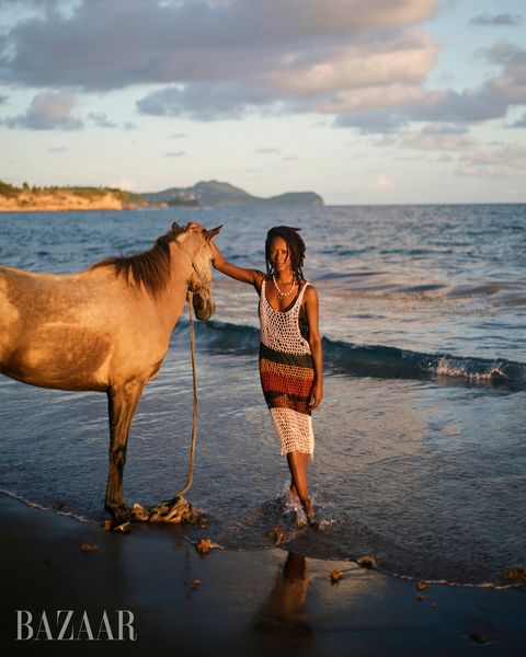 shala monroque stands on the beach beside a tan horse