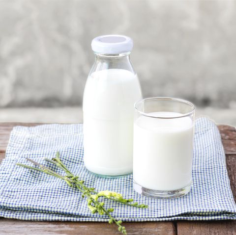 a cup and bottle of milk on a table, an ingredient in one of good housekeeping's best homemade face scrubs
