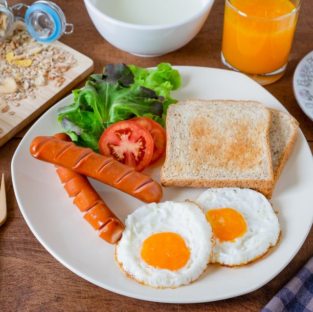 Healthy breakfast with fried eggs, toasts, sausages and vegetable on the white plate. Muesli with yogurt, orange juice, hot coffee on wooden background. Top view and copy space