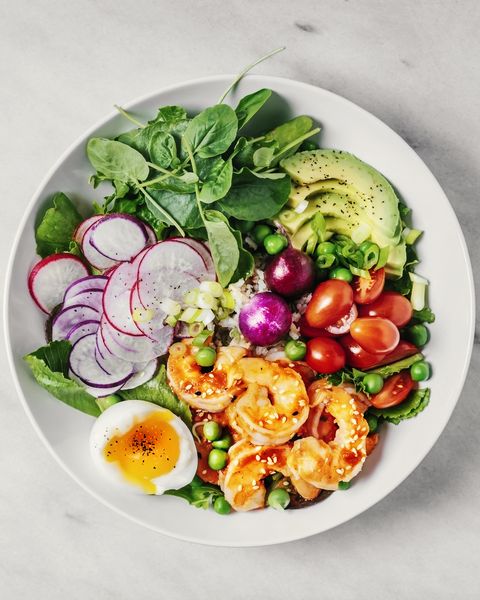 healthy lunch bowl with greens, avocado, cherry tomatoes, radish, boiled egg, and shrimp on white background