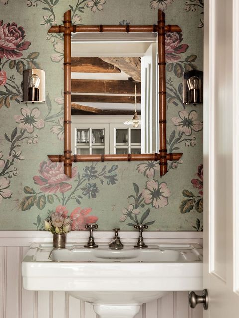 a sink with a bamboo mirror above it against sage wallpaper with florals on it
