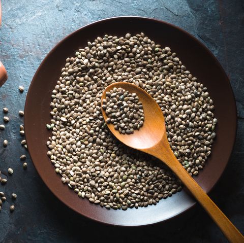 Hemp seeds on a plate and in a sieve on a gray blue stone