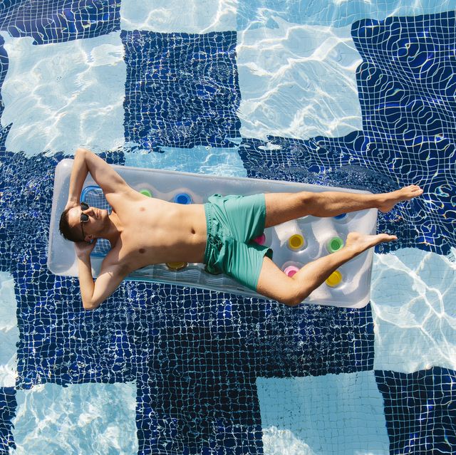 high angle view of a young man in sunglasses sunbathing in swimming pool on inflatable pool raft