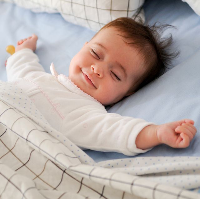 una niña duerme tranquila en su cuna con una sonrisa