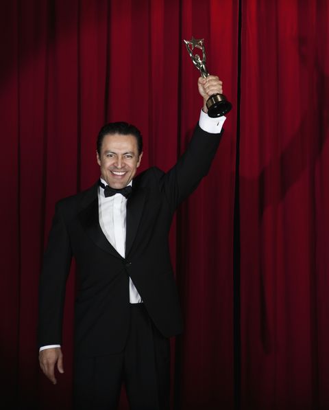 hispanic man in tuxedo holding trophy onstage
