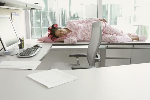 Hispanic woman in pajamas and curlers sleeping on her desk