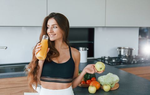 holds apple in hand young european woman is indoors at kitchen indoors with healthy food
