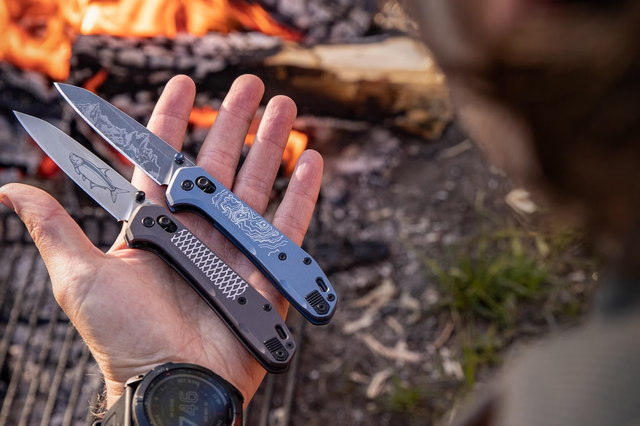 a hand holding two pocket knives in front of a fire