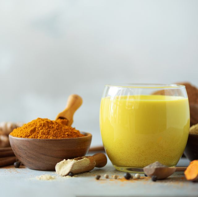 Hot healthy drink. Turmeric latte, golden milk with turmeric root, ginger powder, black pepper over grey background. Copy space. Spices for ayurvedic treatment. Alternative medicine concept.