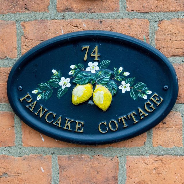 house sign      oval metal wall mounted house sign for pancake cottage, olney, buckinghamshire references the famous pancake race which takes place in the town