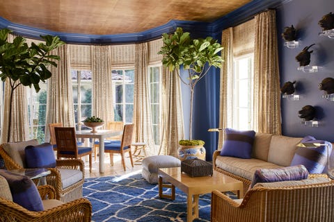 fortuny barkcloth and cotton fabrics cover wicker seating and windows respectively   in the deep blue sunroom