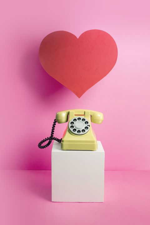 Teléfono amarillo con un corazón de amor rojo sobre fondo rosa
