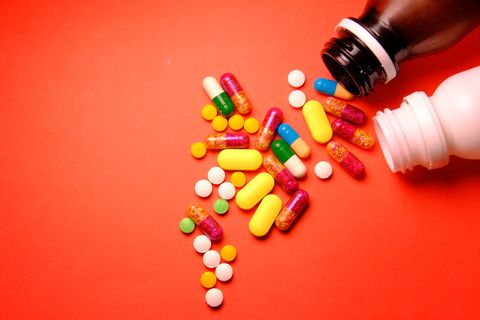 Bottle of medicine with random pills scattered on a red-orange surface.