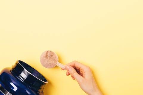 eat for abs view from above female hand takes spoonful of protein powder from jar on yellow background with copy space