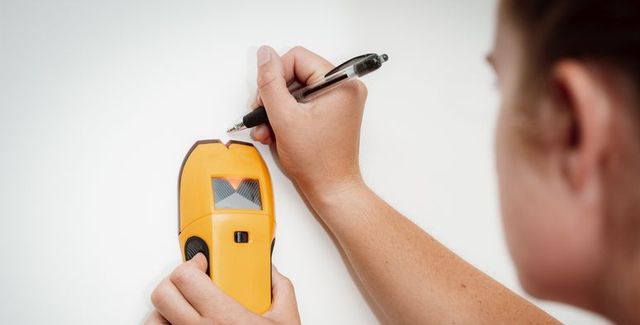 a women uses a stud finder on a wall and marks the location for a diy home project